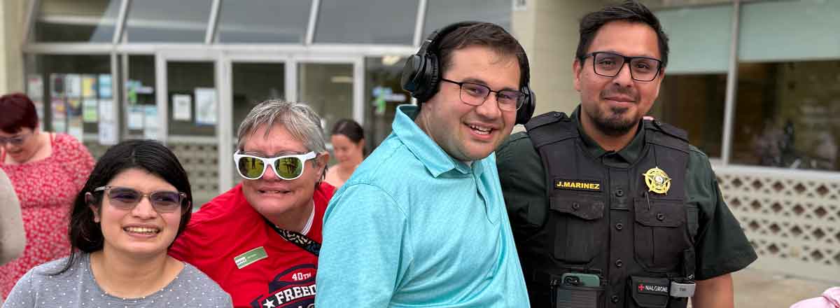 a group of smiling special needs adult with a police man, all are happy to meet the policeman and pose for a picture
