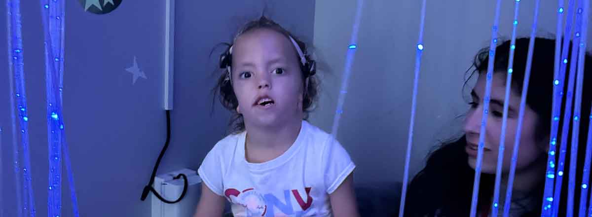 A photo of a special need young girl in the SRACLC sensory room, glowing lines of lights softly glow around her