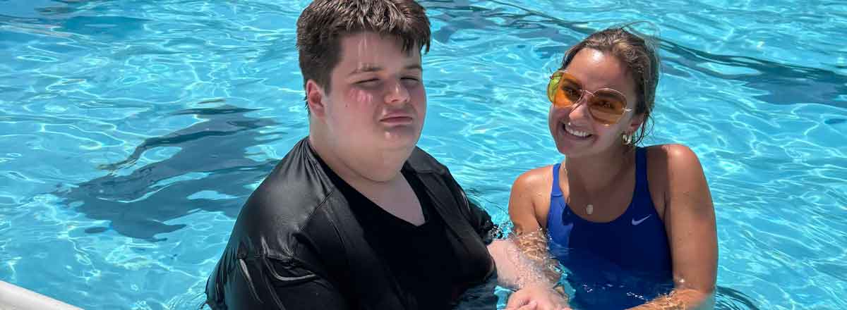 This is a photo of a special needs male adult in the pool with teh SRACLC staff smiling, teh sun is shining and reflecting off teh wtaer