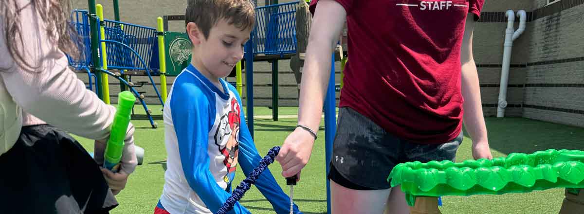 a young special needs boy smiling as his bucket get fills with water on teh playground