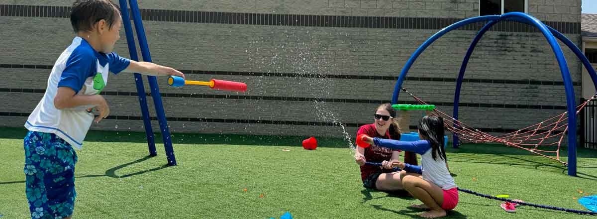 two smiling Special needs children and SRACLC staff member having a water squirt fight on the playground, the sun is shining