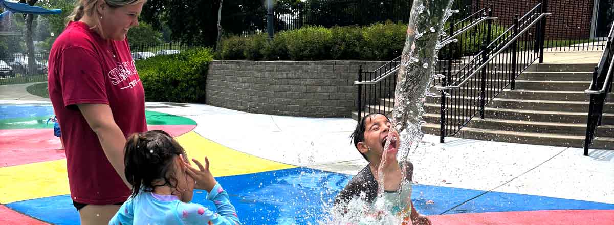 special needs children playing at a splash pad a little boy smiling as the water form the waterfall falls onto his face