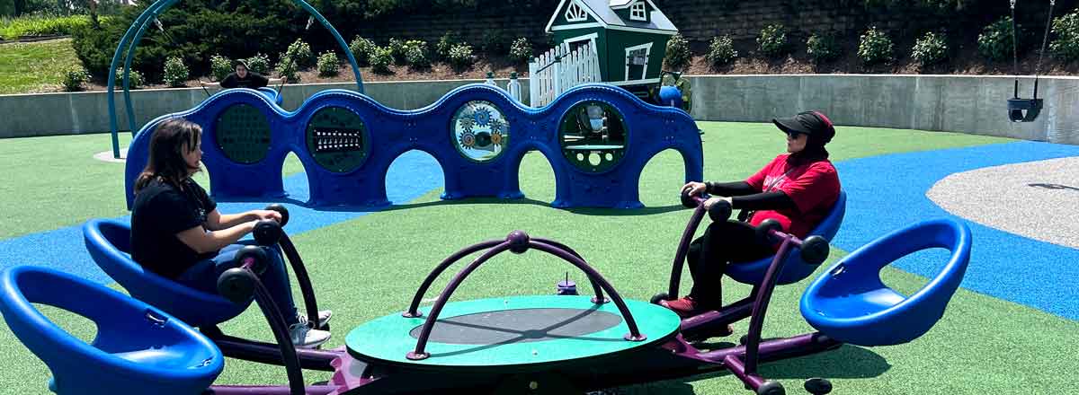 two adult special need sitting on a adult sized tetter-totter at a local playground
