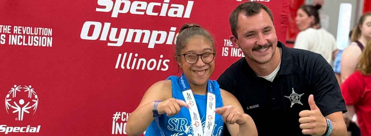 special needs athlete posing with her coach at the special Olympics with her metal around her neck, her smile beams