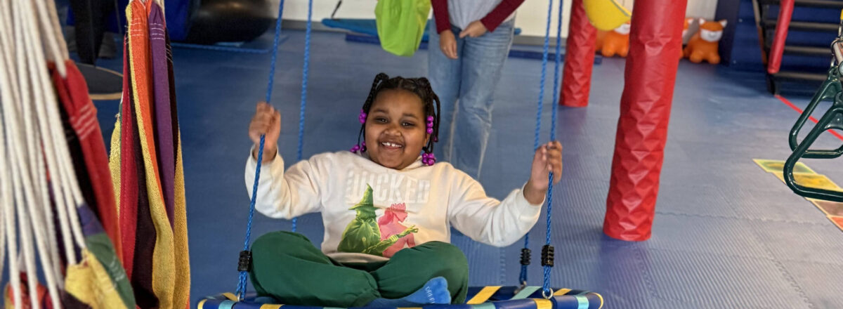 sraclc-adaptive-recreation-indoor-swing A child enjoys swinging on an adaptive chair swing inside a gymnasium.